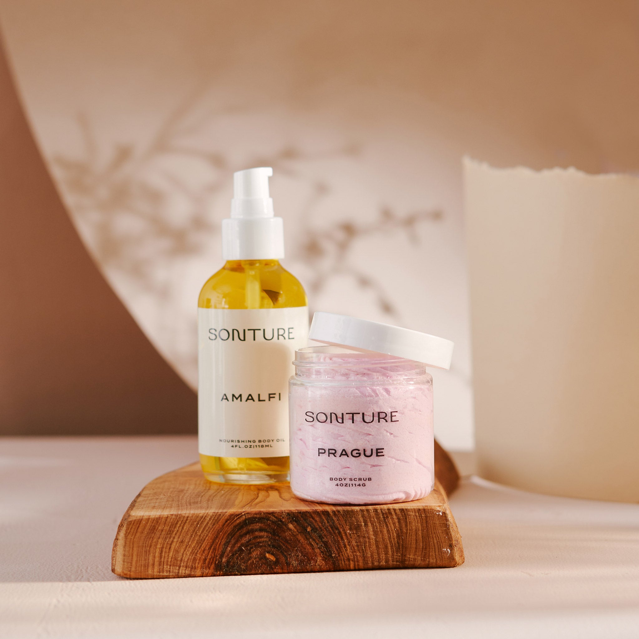 A Sonture handmade whipped body butter and luxurious body oil is styled on a wooden board in a beautiful beige setting. The elegant products are inspired by exotic travel destinations and feature ethically sourced ingredients. 