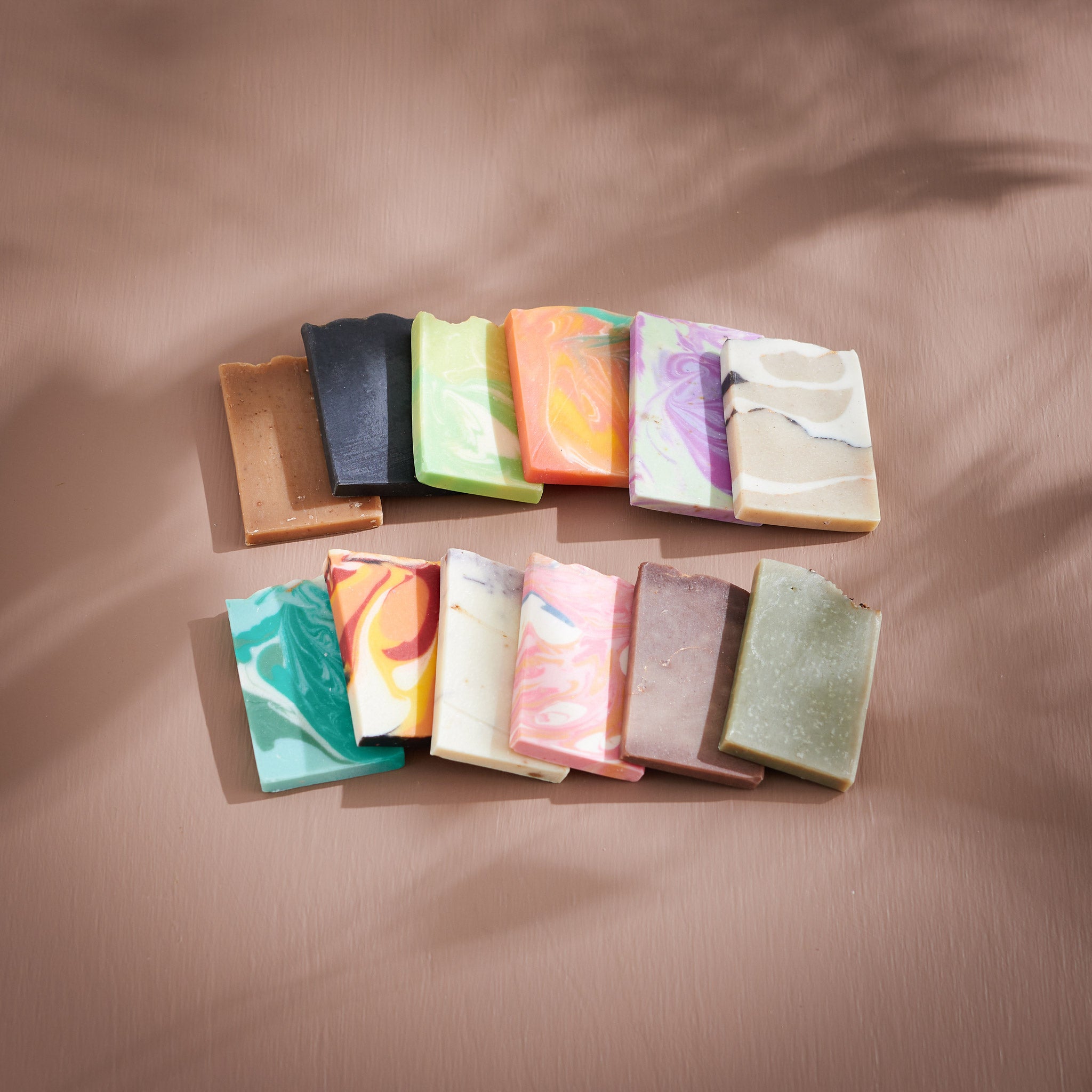 A range of Sonture's handmade soaps sit flat as part of the sample pack in a lightly shadowed beige background. The soaps feature warm colours and gold swirls.