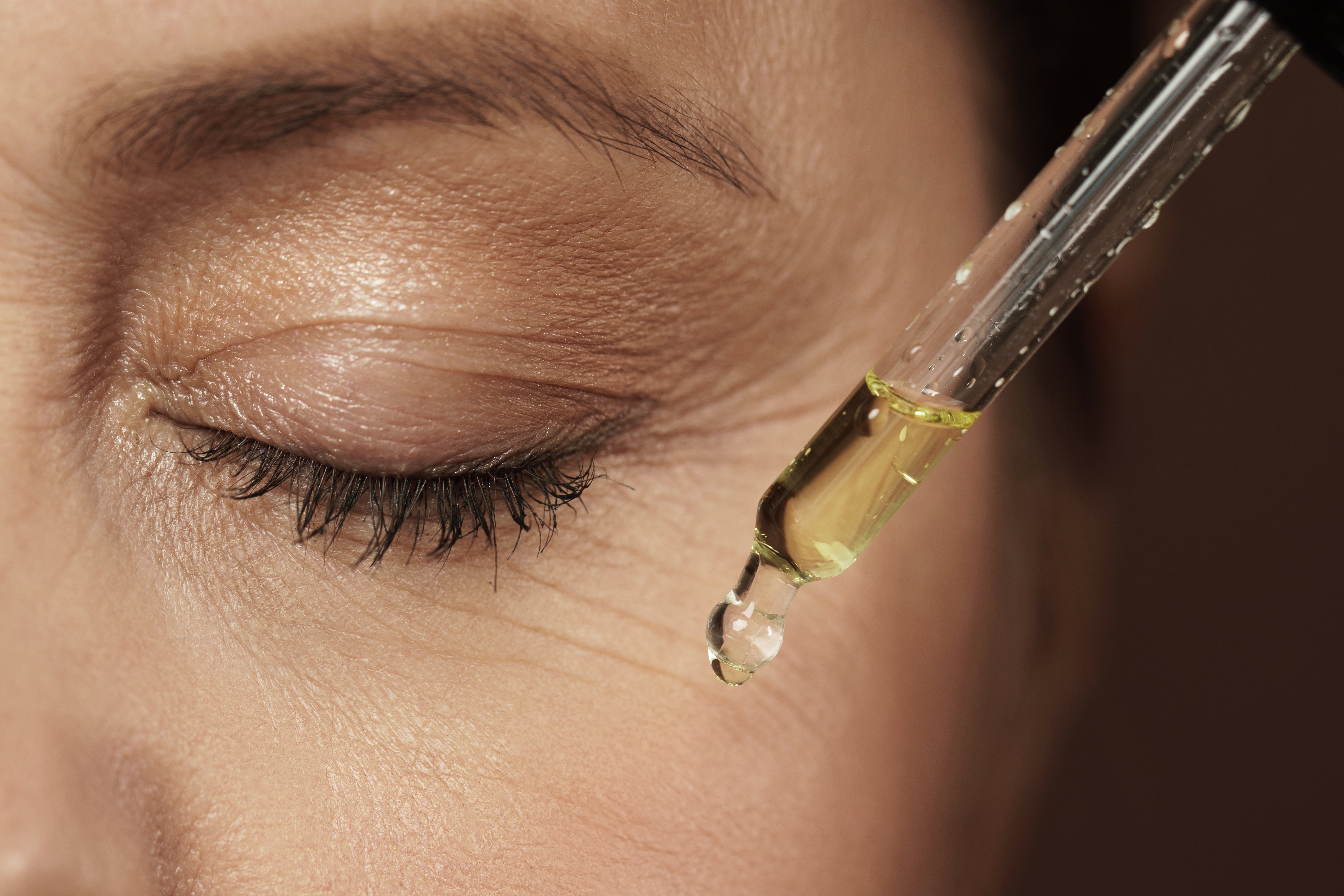 Closed eye of mature woman with oil dropper.