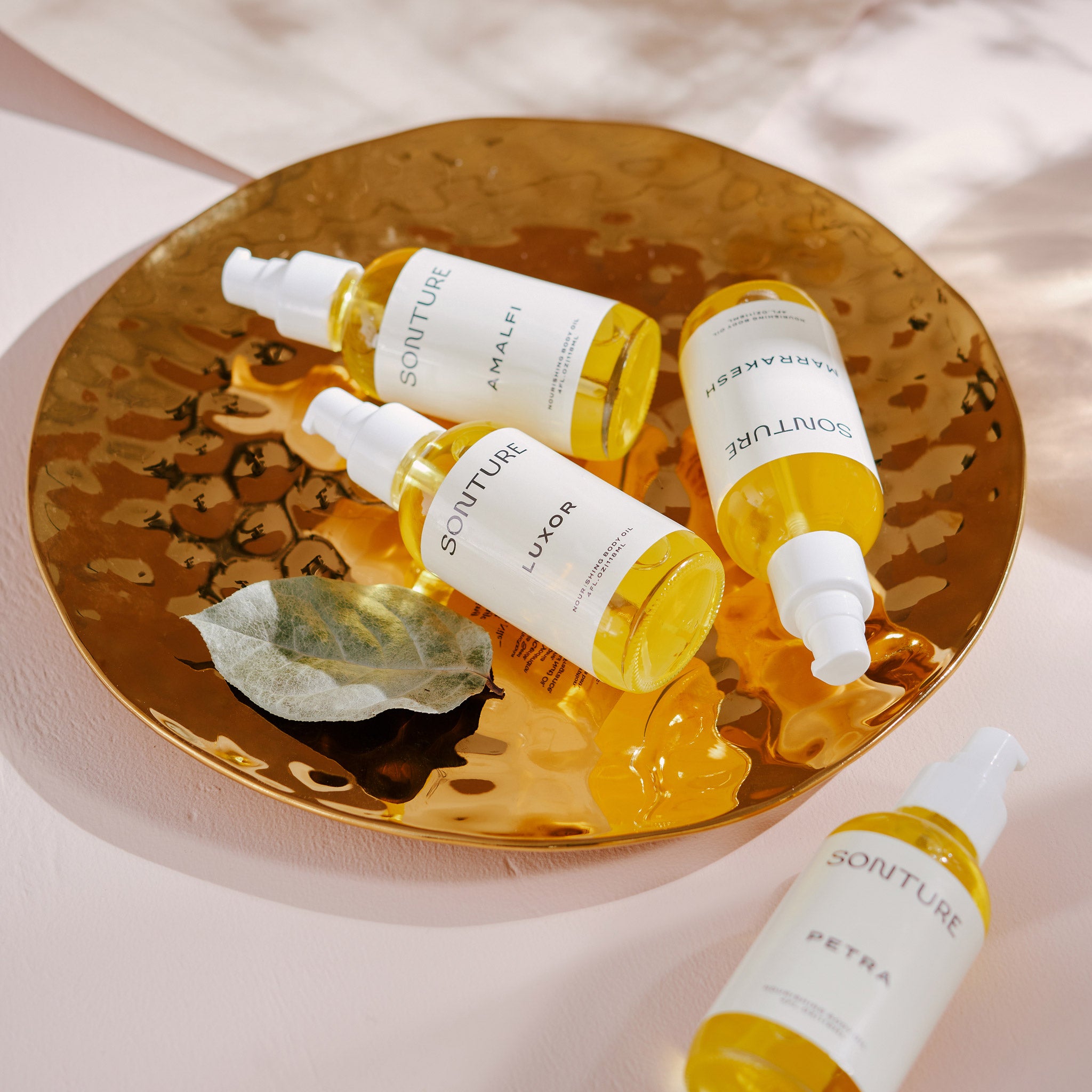 Sonture’s collection of luxurious handmade body oils sit on a gold disk on a shadowy white tabletop. The products are inspired by exotic travel destinations and feature ethical time-honoured ingredients.