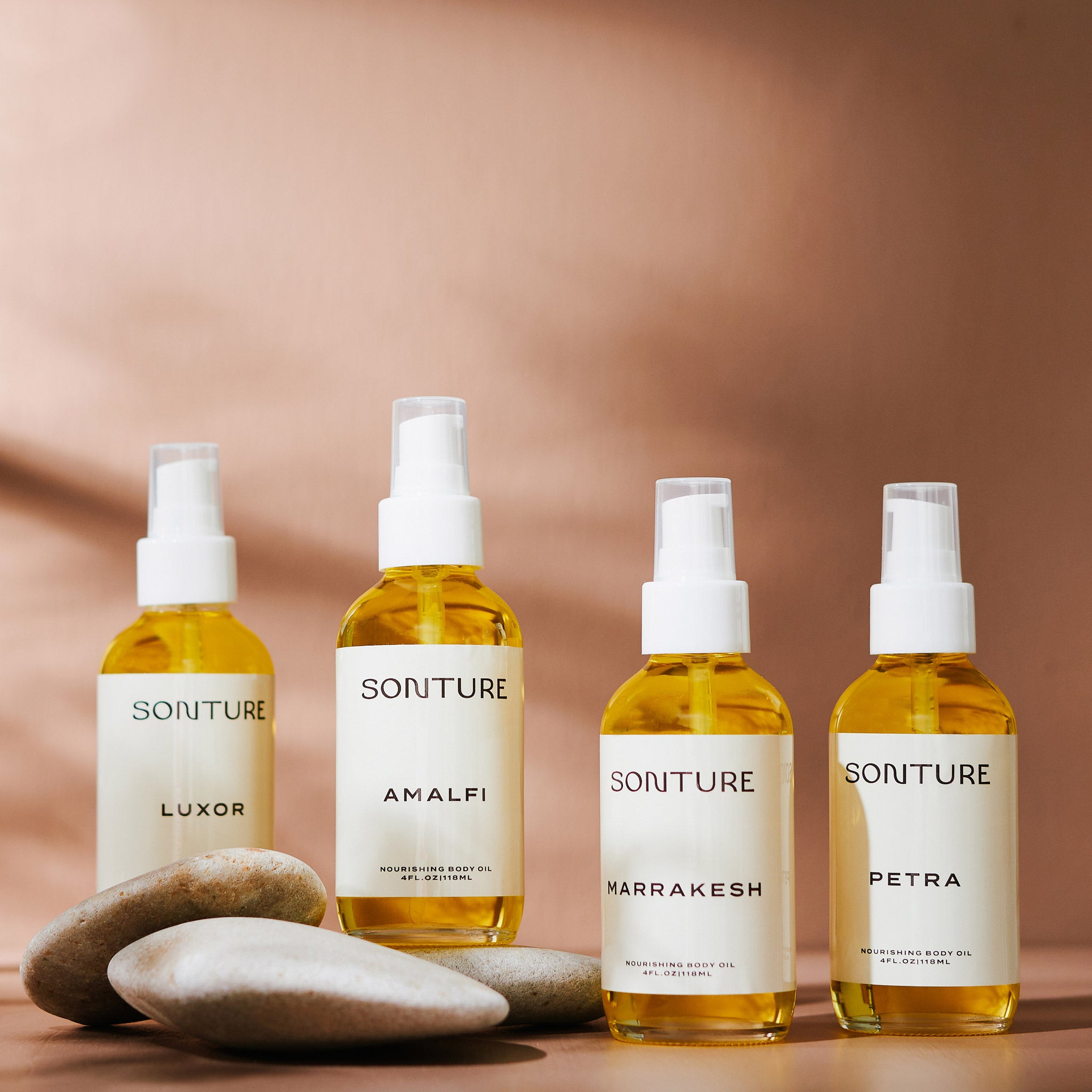 The full collection of Sonture’s handmade body oils sit in a shadowy beige setting styles with smooth stones. The clear glass bottles show the rich yellow oil with the cream labels featuring sophisticated brand design.