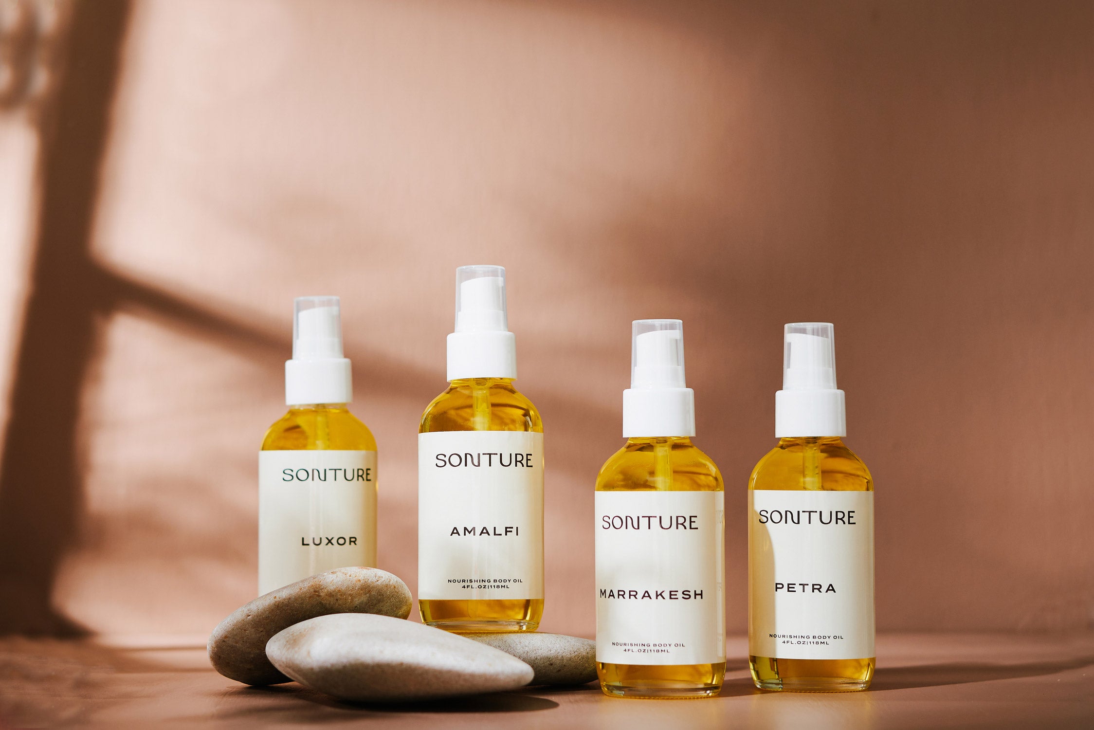 Sonture Luxurious Face and Body Oils are handcrafted in New York with Ethically made ingredients. The four travel inspired products are in glass bottles with white cream labels and sit with smooth stones in a rich beige background.