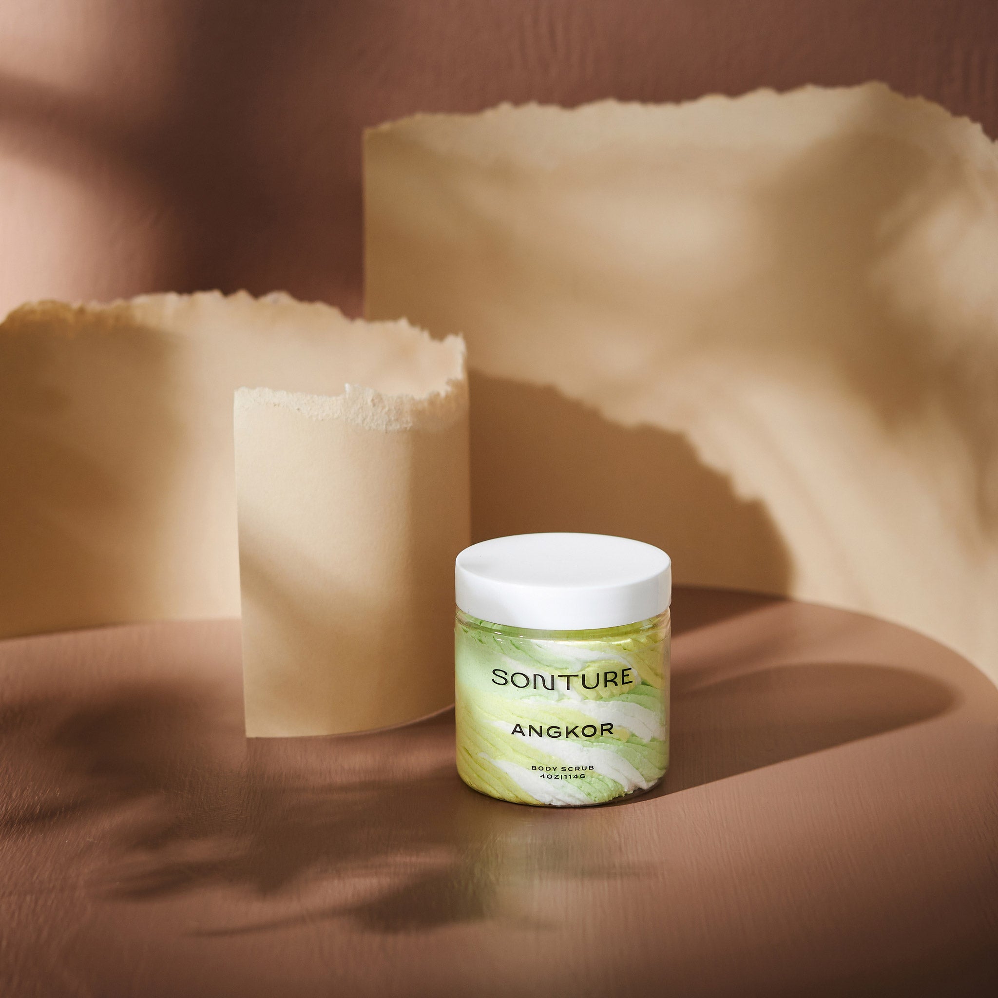 Sonture body scrub Angkor sits in a beige background with paper styling. The packaging is clear so as to show the product detail and the ethically sourced handmade nature of the travel inspired product.