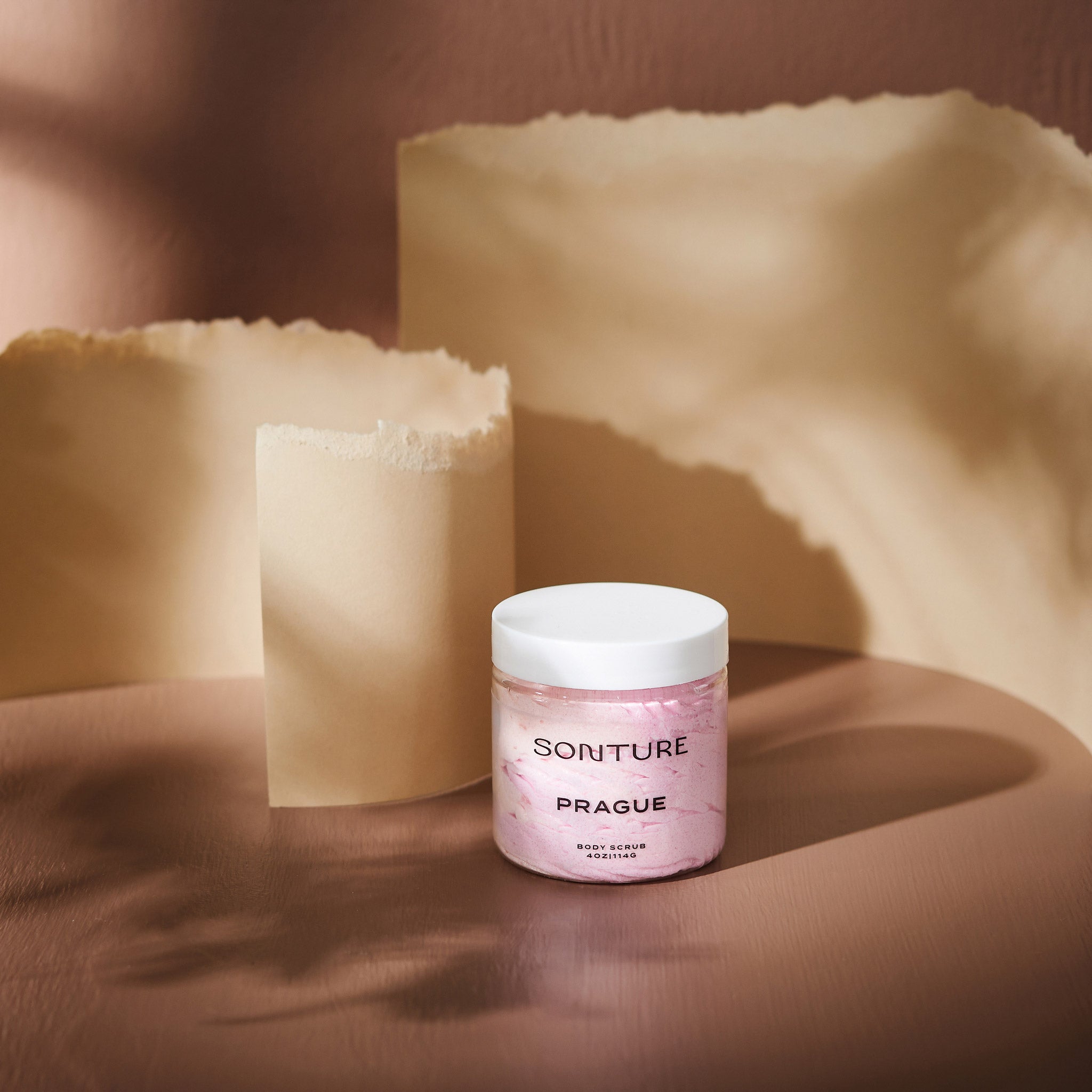 Sonture body scrub Prague sits in a beige background with paper styling. The packaging is clear so as to show the product detail and the ethically sourced handmade nature of the travel inspired product.