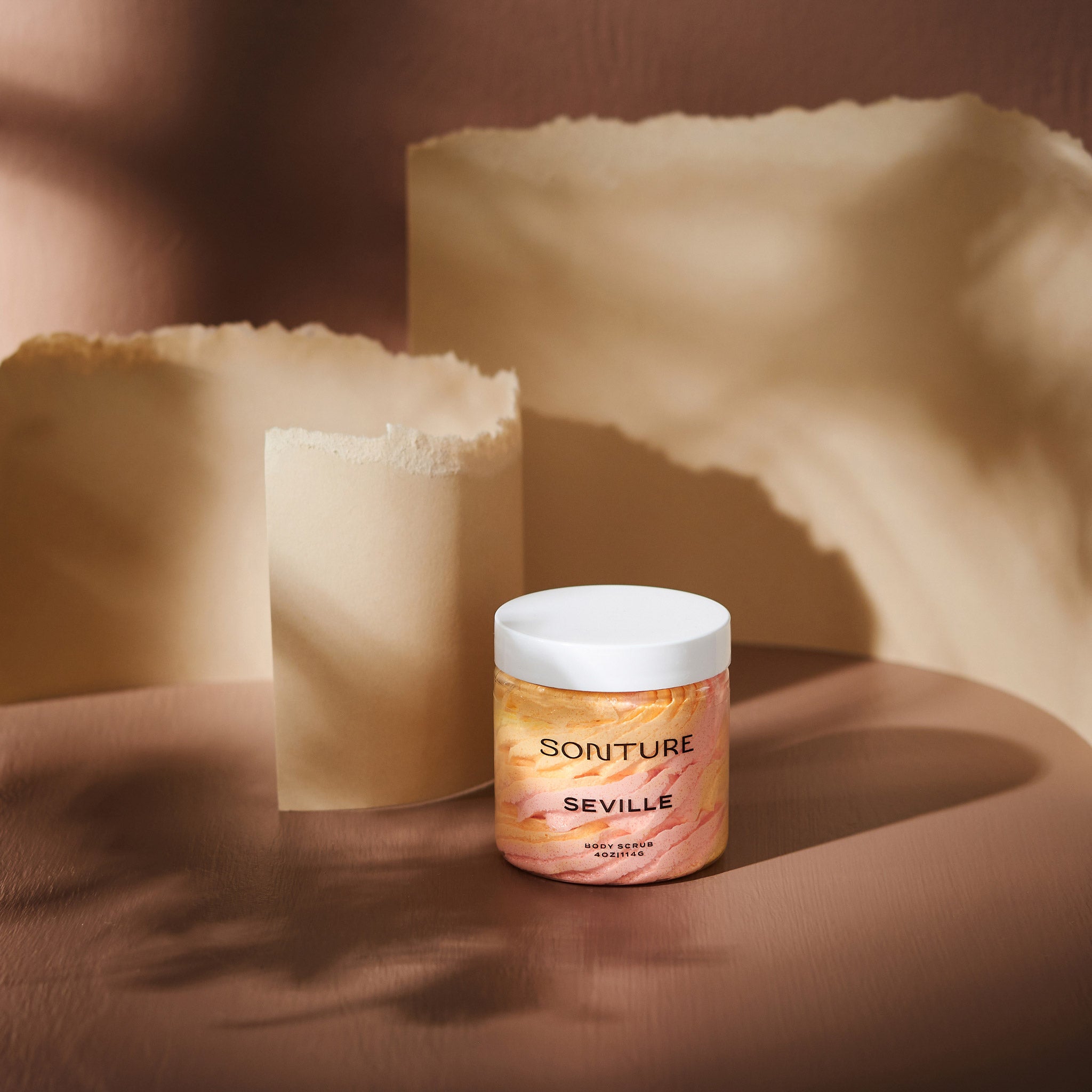 Sonture body scrub Seville sits in a beige background with paper styling. The packaging is clear so as to show the product detail and the ethically sourced handmade nature of the travel inspired product.