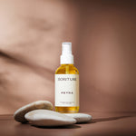 Sonture’s Petra Nourishing handcrafted body oil is travel inspired and features ethical ingredients. Here the luxurious self care product sits in glass packaging with a cream label in a shadowy beige background.