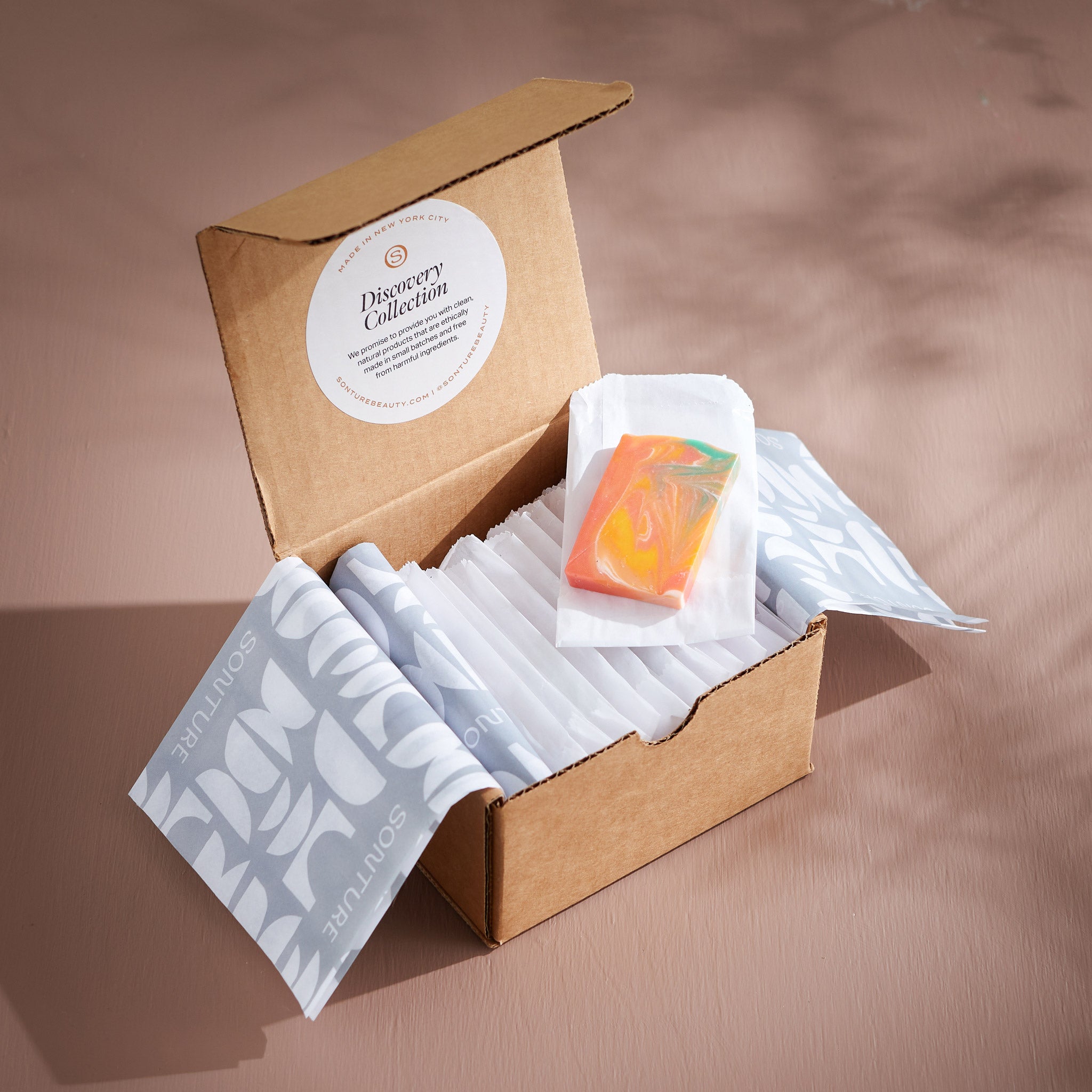 The Sonture Discovery Collection is a small box of soap samples showcasing the ethical ingredients and high quality handmade soap. The samples are individually wrapped and secured with lush tissue paper and sit in a warm tan background.