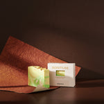 Sonture’s Osaka handcrafted natural soap bar is inspired by travel and features nourishing natural ingredients. Here the luxurious self care product sits in a cream coloured box with a diet in a deep chocolate brown background with rust red paper. 